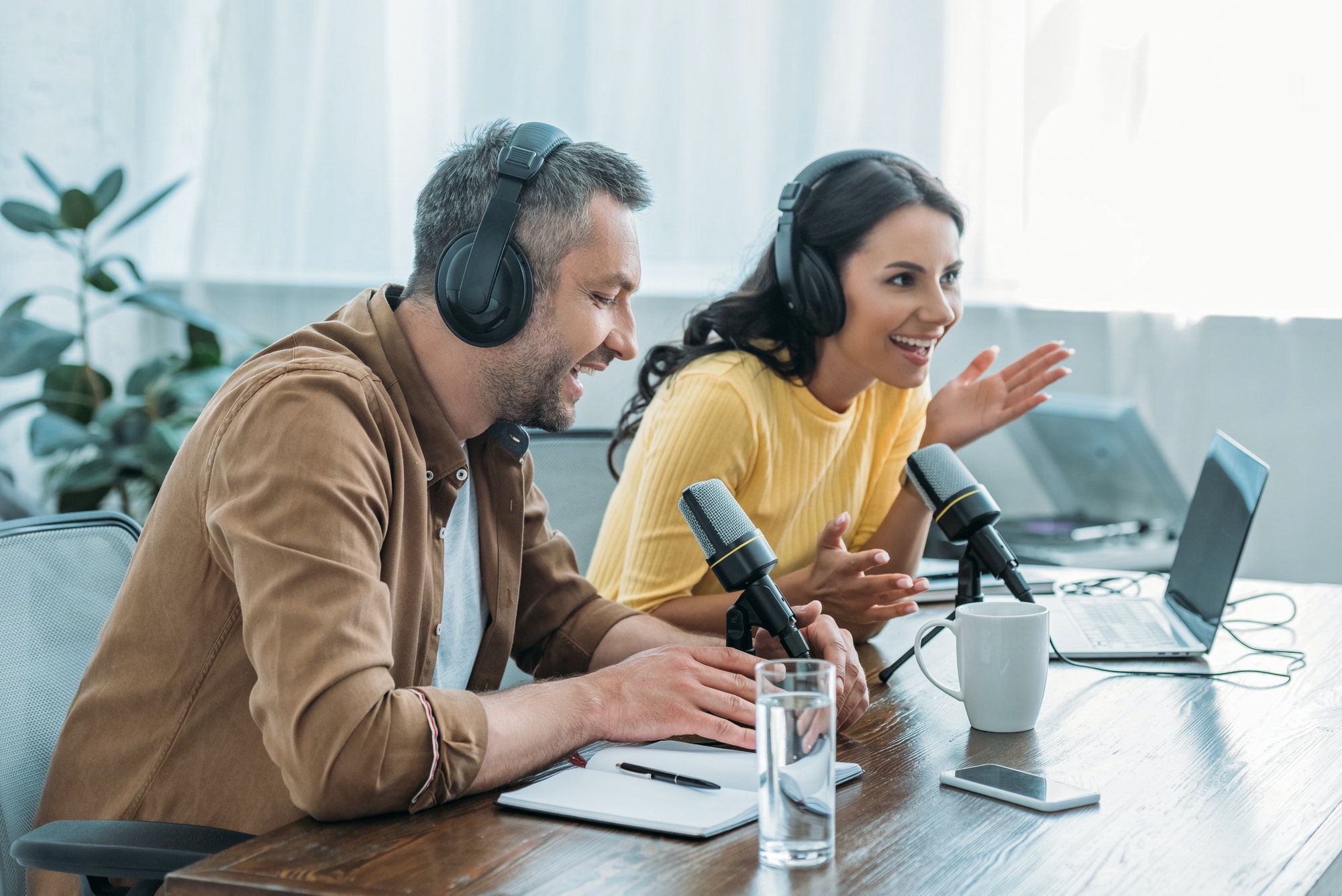 two cheerful radio hosts in headphones recording podcast in studio